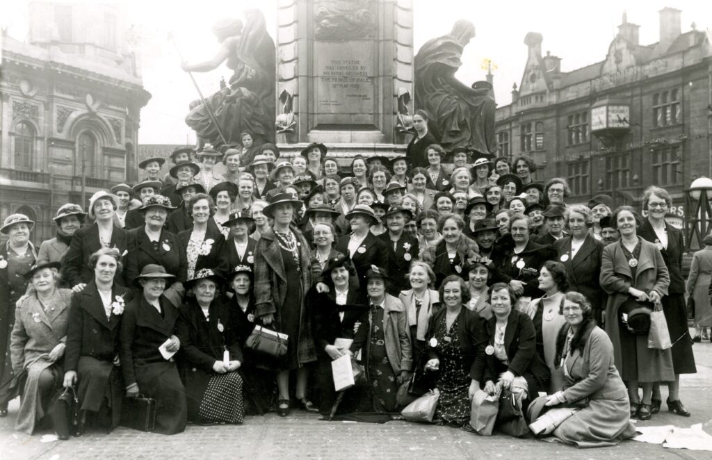 Black and white image of a group of women in 1930s dress grouped around a statue.