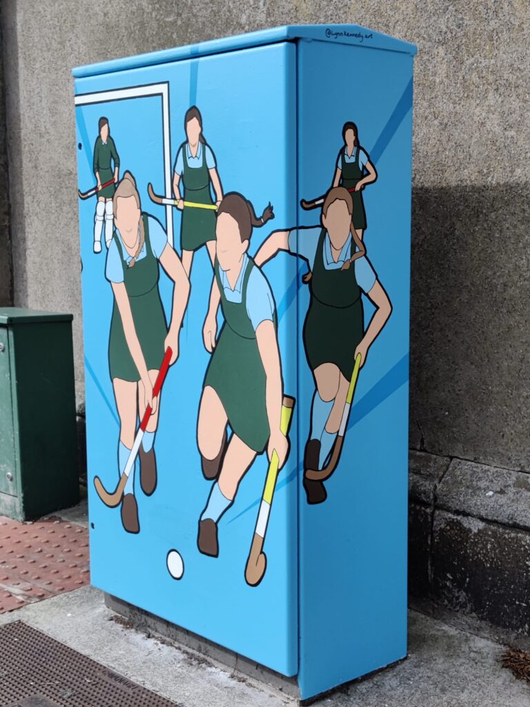 painted traffic light control box depicting stylised illustration of girls playing hockey.