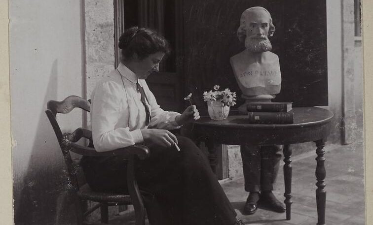 Margaret Hardie pictured on the Finlay terrace at the BSA around 1911-12. She sits on a chair, foot on stool. Flowers and books on the table.